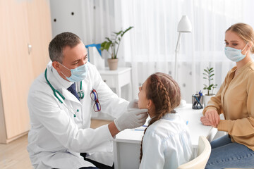 Doctor examining little girl with sore throat in clinic