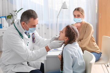 Doctor examining little girl with sore throat in clinic