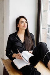 Portrait of a happy mid adult woman sitting by window at home. Relaxed woman smiling