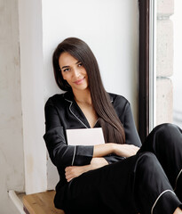 Portrait of a happy mid adult woman sitting by window at home. Relaxed woman smiling
