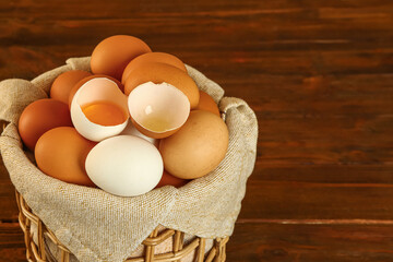 Wicker basket with fresh chicken eggs on wooden background, closeup