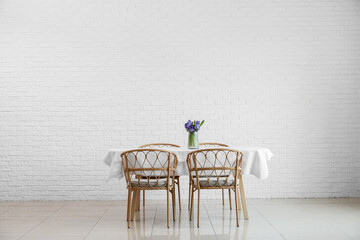 Dining table with flowers and chairs near white brick wall