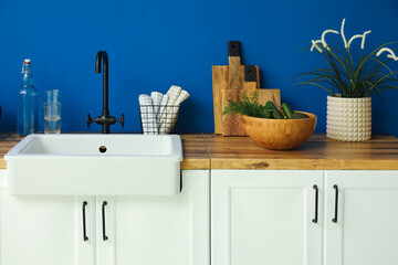 Ceramic sink with kitchen utensils and food on counters near blue wall