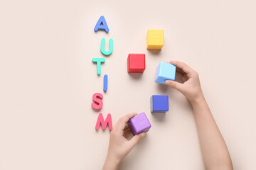 Child with cubes and word AUTISM on beige background