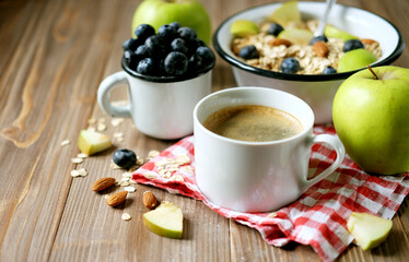 Oatmeal porridge, coffee, apple, berries and nuts on a wooden table.