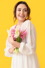 Pretty young woman with hyacinth flowers on yellow background