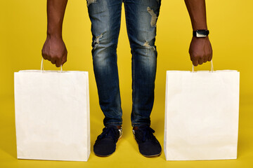In frame, two legs and two hands of black man lifting two white paper bags from the floor on a...