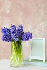 Vase with hyacinth flowers, book and blank photo frame on table near color wall