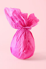 Chocolate Easter egg wrapped in paper on pink background
