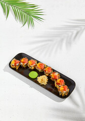 Tempura sushi roll with grapefruit and mango sauce. Hot maki sushi in black plate on white background. Summer menu for japanese restaurant. Modern sushi menu with hard shadow and leaves.