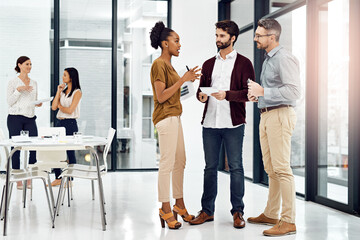 Their input in invaluable. Shot of three businesspeople talking in the office with their colleagues in the background.