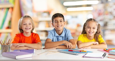 Child  are sitting at a school desk, writing,  his hand up. school classmates are sitting in the classroom