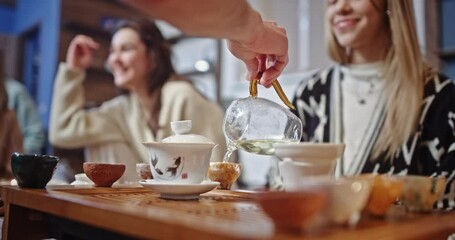 Person pouring an Asian drink into small pottery cups. Person pouring an Asian drink into small pottery cups for a group of friends seatedaround a table on the floor in a close up on his hand and jug