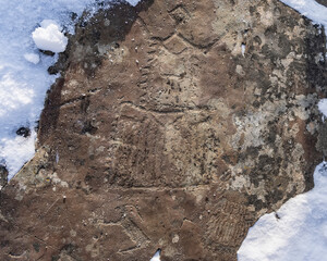 Ancient petroglyphs are carved on the stone. Mysterious drawings on a weathered surface overgrown...