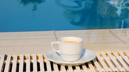 White cup of coffee or hot drink on the background of a blue swimming pool on a summer sunny day. Good morning concept and planning a new day, week, month. Vacation and travel. copy space