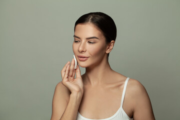 Fototapeta premium Attractive woman removing makeup with white cotton pad on gray background