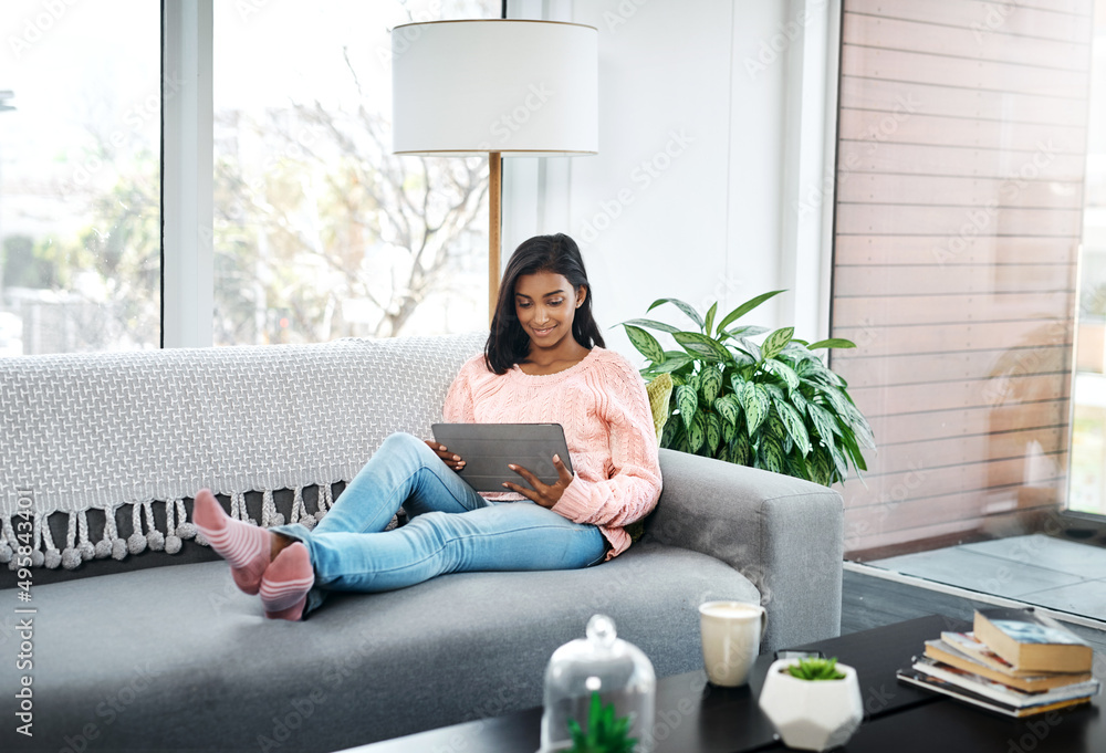 Poster What I prefer to do on the weekend. Cropped shot of a beautiful young woman using a tablet while chilling on the sofa in the living room at home.