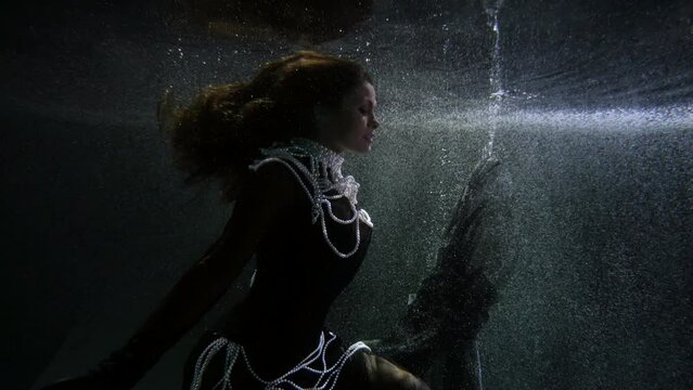 A pretty girl in a black dress with white pearls underwater immersion in the fantasy of weightlessness and sleep