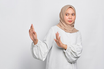 Serious young Asian Muslim woman makes stop gesture and demonstrates rejection isolated over white background