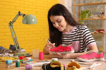 Woman painting on sneaker at wooden table indoors. Customized shoes