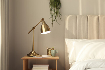 Stylish golden lamp and stationery on wooden nightstand in bedroom. Interior element