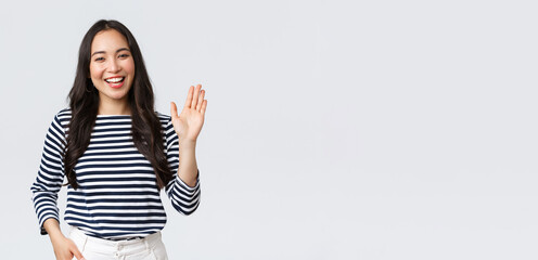 Lifestyle, people emotions and casual concept. Friendly cheerful asian woman smiling, saying hi and waving hand to greet person, make hello gesture, welcome someone