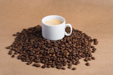 Small white coffee cup with espresso crema on roasted beans at brown background. Mock up