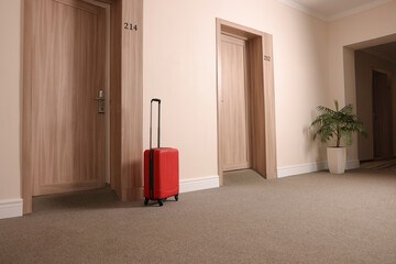 Modern red suitcase in empty hotel corridor
