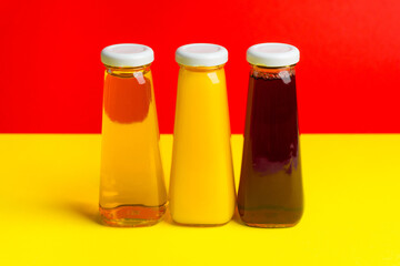 Bottles with yellow and red liquid halthy beverage on yellow background. Orange apple cherry juice