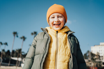 Portrait of happy laughing child boy on the beach. Kid smiling outdoors on the autumn winter beach