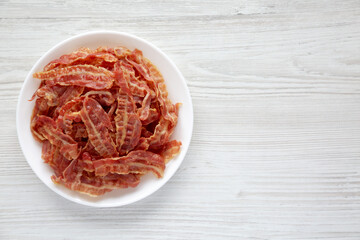 Crispy Fried Bacon on a white plate on a white wooden background, top view. Flat lay, overhead, from above. Space for text.