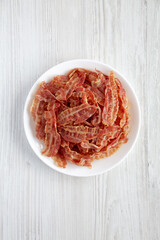 Crispy Fried Bacon on a white plate on a white wooden background, top view. Flat lay, overhead, from above.