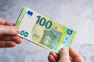 Hands holding and giving one hundred euro banknotes. Stack of money in man hands on gray background