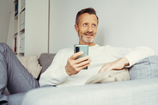 older man with cell phone sits at home on sofa and looks to the side