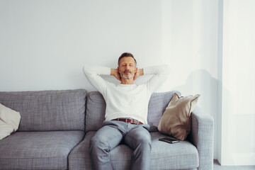 older man sitting at home on sofa with arms relaxed behind head