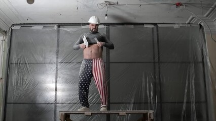Fat bearded adult man in protective helmet and USA flag print on pants remove construction whitewash vintage high ceiling. Overhaul repair with your own hands concept. 4k slow motion footage 