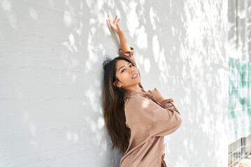 woman dancing back to white wall with plant shadows and hand raised