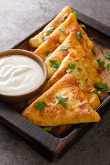 Ukrainian triangular fried pancakes benderyki served with sour cream close up on a wooden tray on the table. Vertical