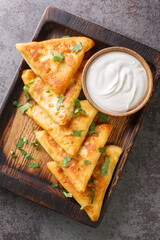 Ukrainian triangular fried pancakes benderyki served with sour cream close up on a wooden tray on the table. Vertical top view from above