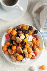 Assorted nuts, dried fruits and candied fruit. In a white plate. Close-up. Light background. View from above.
