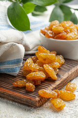 Golden raisins are scattered on the board. In the background are raisins in a plate and greens. Close-up. Light background.