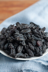 Black raisins on a white plate. On a blue napkin. Close-up. Macro.