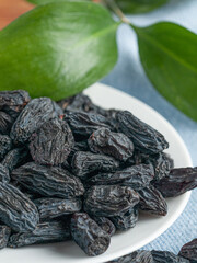 Black raisins on a white plate. On a blue napkin. Close-up. Macro.