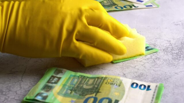 Laundering of money. Man in yellow gloves washes papper hundred 100 euro with green washcloth