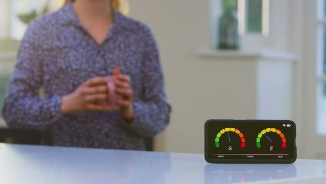 Close Up Of Woman With Drink Picking Up Smart Energy Meter Measuring Electricity And Gas Use At Home - Shot In Slow Motion