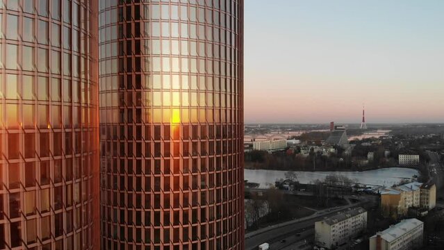 Beautiful drone view of clear pink sky and Riga, Latvia cityscape on a golden sunset with twin Zunda towers skyscrapers in foreground reflecting the sun.