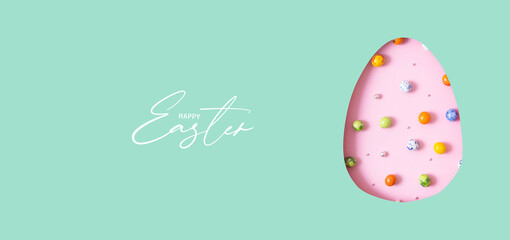 Happy Easter text with Easter egg cut out of paper and chocolate mini eggs. Creative Easter holiday greeting card banner format
