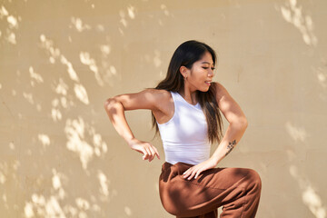 Woman dancing in front of warm beige wall kneeling