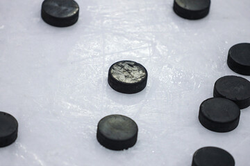Multiple black Ice Hockey pucks laying on Ice rink ground.