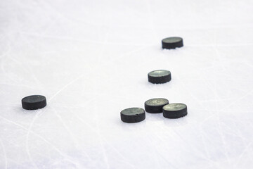 Multiple black Ice Hockey pucks laying on Ice rink ground.